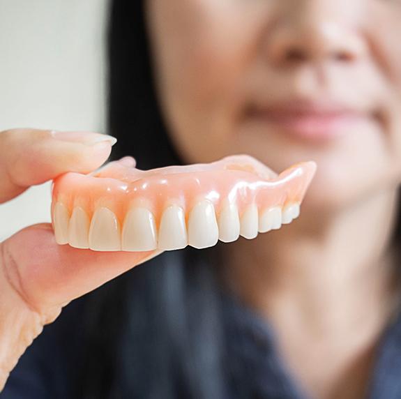 Woman blurry in background holding upper arch of dentures to foreground
