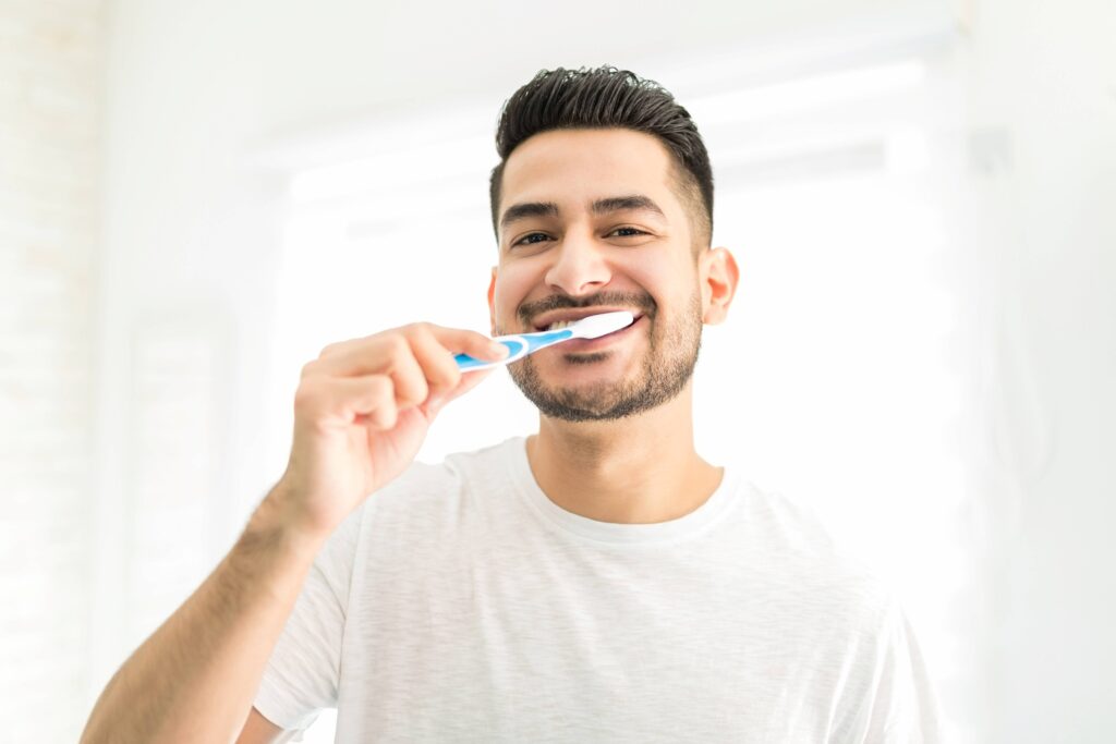 Man smiling while brushing his teeth in bathroom