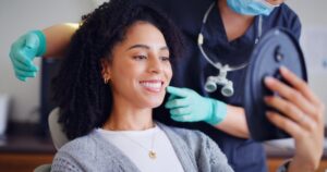 Woman smiling and looking into handheld mirror in dentist's chair. 