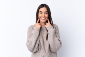 Woman in a beige sweater pointing at her straight teeth